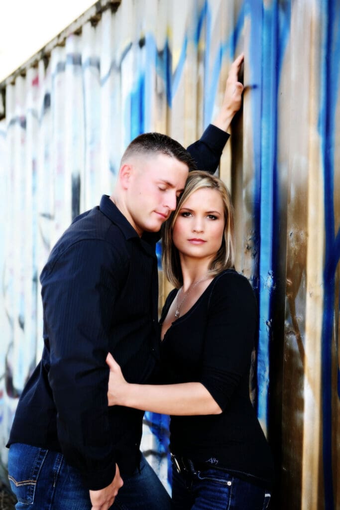 Engaged couple posing together against a colorful graffiti wall during an urban downtown Portland engagement session photographed by Tobi Rose Photography