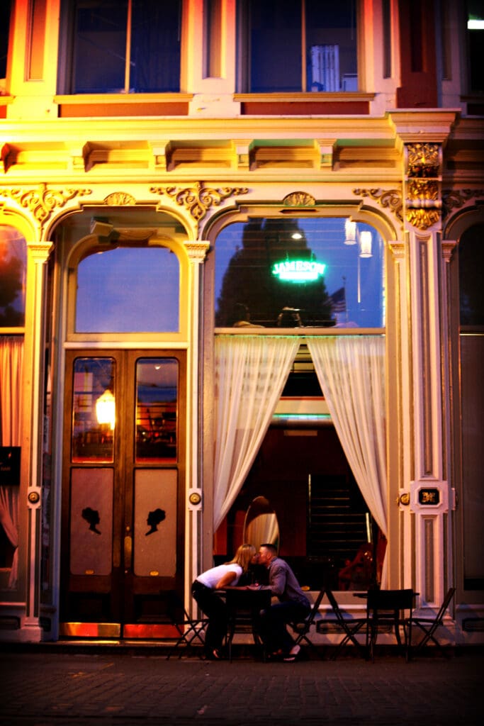 Engaged couple sitting together in a warmly lit doorway at night during a downtown Portland engagement session photographed by Tobi Rose Photography