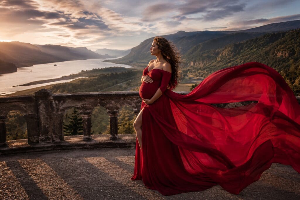 Pregnant woman in a flowing red maternity gown at Rowena Crest Viewpoint overlooking the Columbia River and Columbia River Gorge National Scenic Area in Oregon
