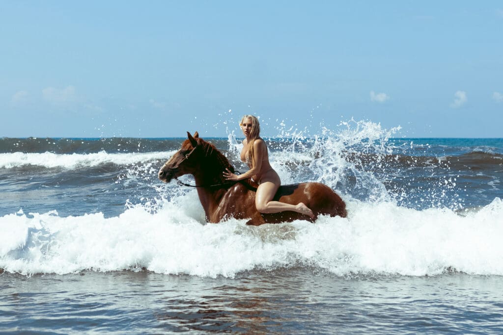 Tobi Rose Rabaliati riding a horse through crashing ocean waves during a Costa Rica beach boudoir session photographed by Marco Ibáñez.