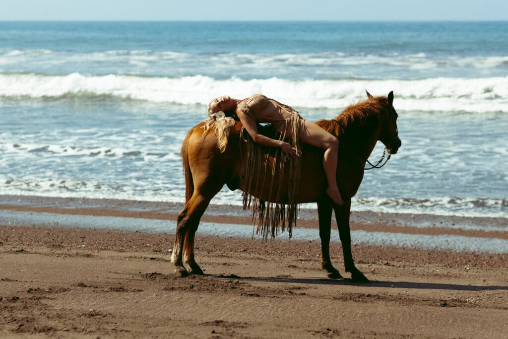 Tobi Rose Rabaliati draped backward across a horse on a Costa Rica beach during a boudoir session photographed by Marco Ibáñez.