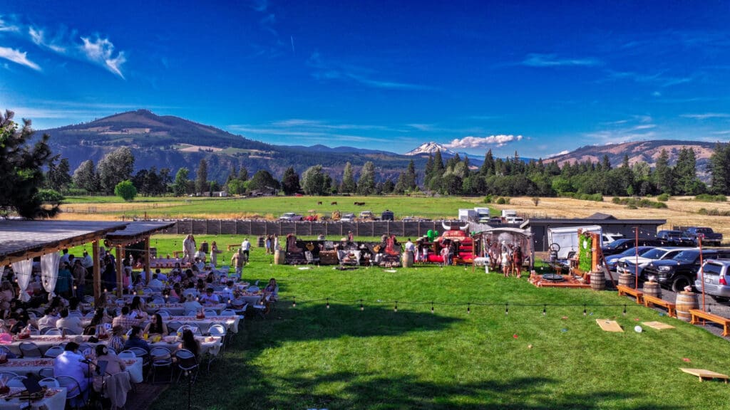 Aerial drone photograph of Letty’s 50th birthday party in Hood River, Oregon, featuring guests, a mechanical bull, photo booths, food vendors, live music and Mount Adams in the background, photographed by Tobi Rose Photography.
