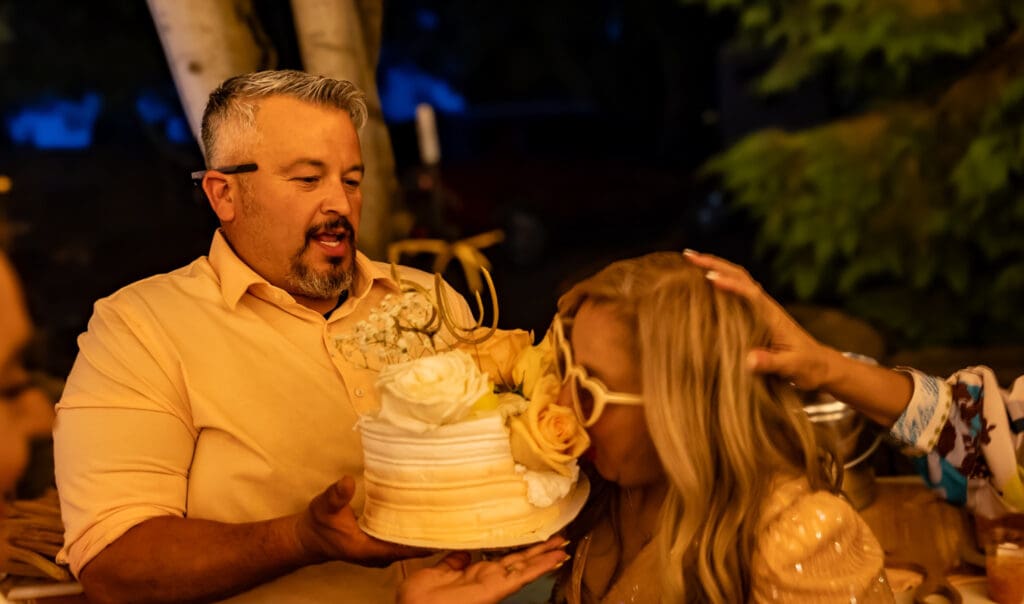 Letty laughing as her best friend pushes her face into her birthday cake during her 50th birthday party in Hood River, Oregon, photographed by Tobi Rose Photography.