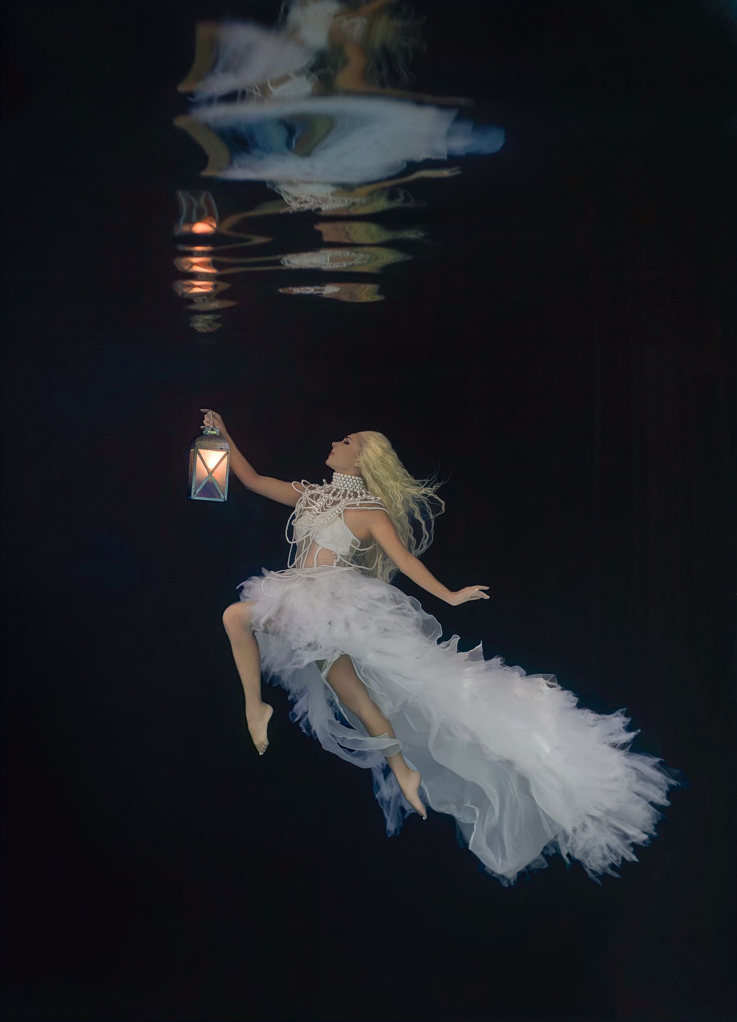 Fine art underwater portrait of Hannah Fraser, known as Hannah Mermaid, in a flowing white dress holding a glowing lantern, photographed by Tobi Rose Rabaliati