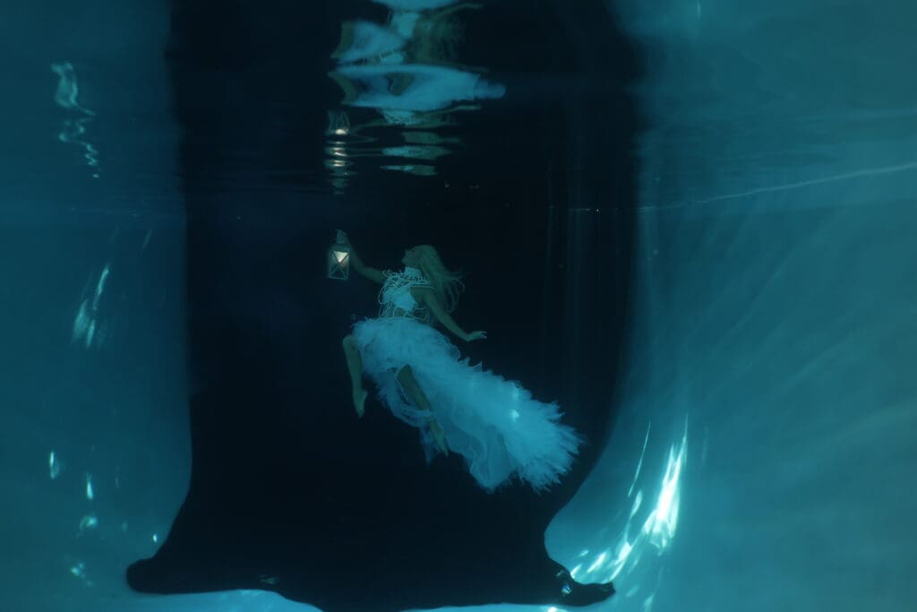Unedited RAW underwater portrait by Tobi Rose Rabaliati showing a woman in a flowing white dress holding a lantern underwater